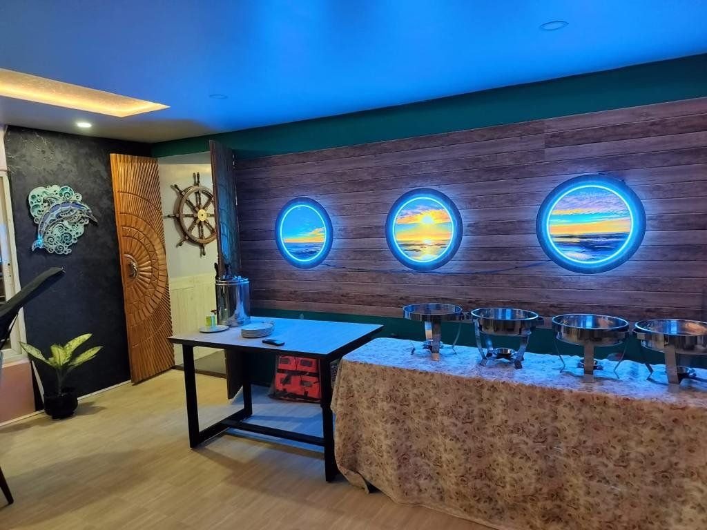 The buffet set up along one side of the saloon: chafing dishes on a skirted table against a timber-clad wall lit by three backlit porthole panels.