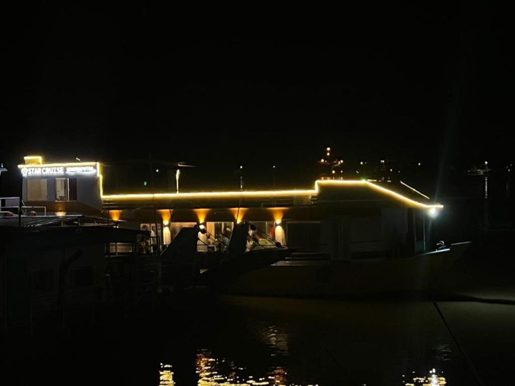 Star Cruise lit up after dark at her mooring, deck lights reflecting off the water.